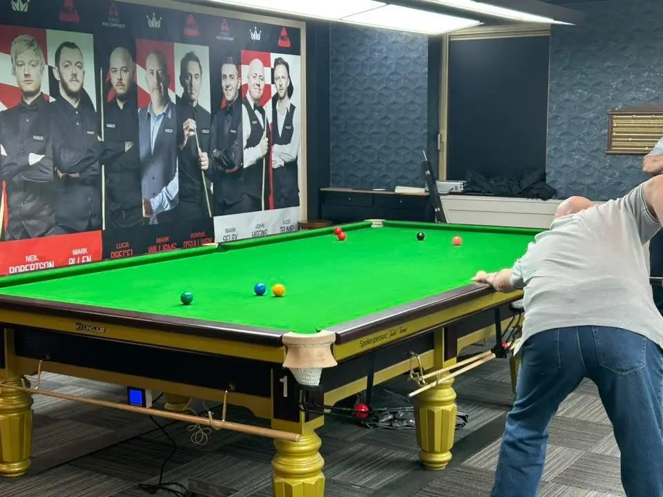 A player leaning in to strike, with a mural of professional players behind the table