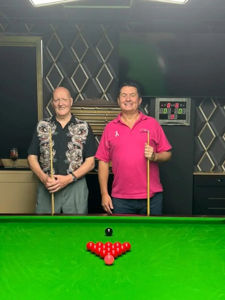 Two players standing behind a freshly racked table with their cues, ready to start