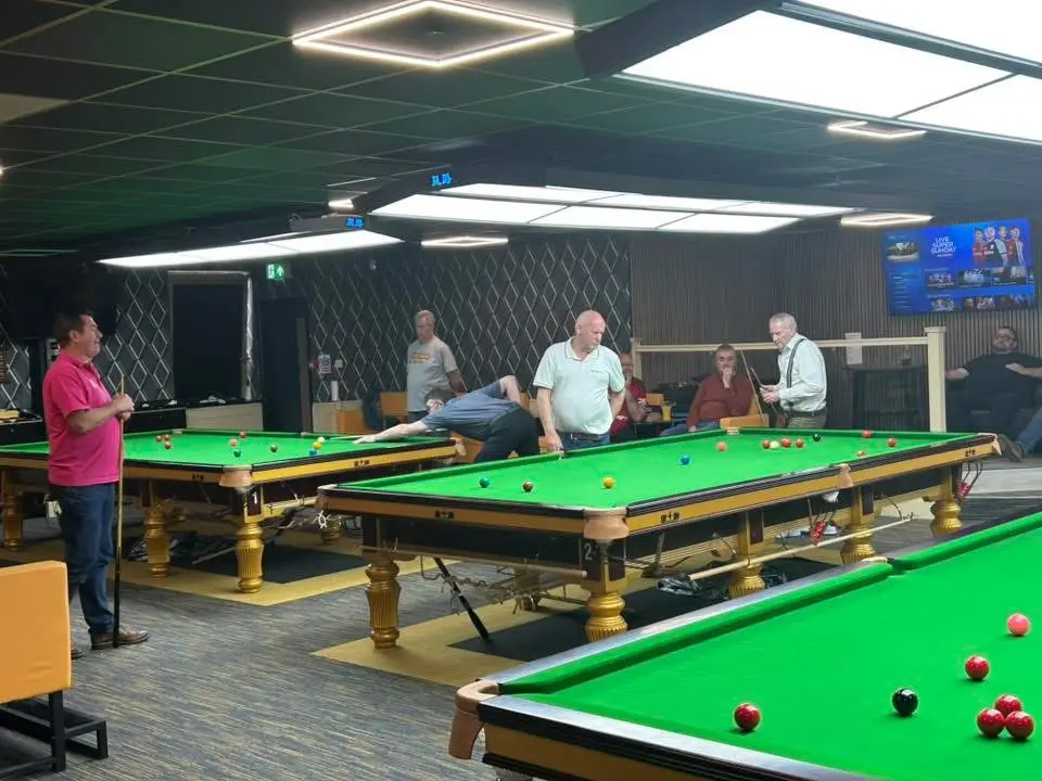A player stretched across the table to reach a shot while others wait their turn