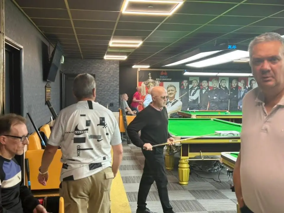 A player carrying his cue between tables as a match goes on behind him