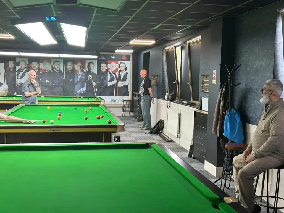 Two players at the table with a spectator watching from a stool at the side of the room