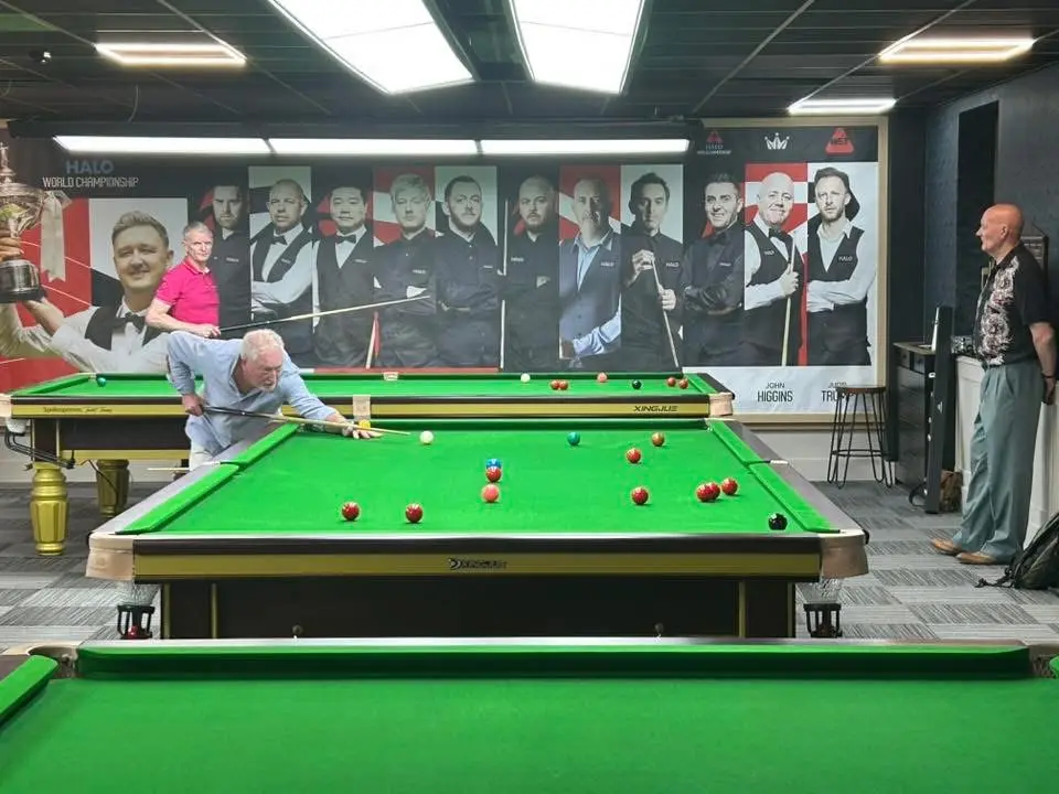 A player leaning across the table to cue, with a spectator standing to one side