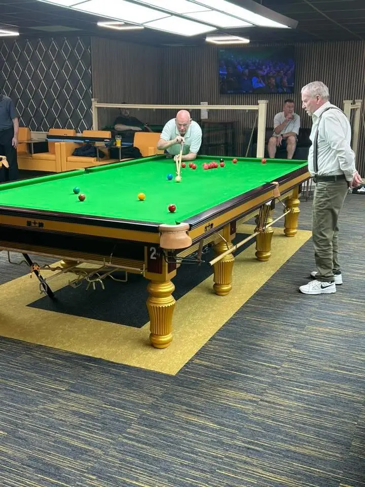 A player at the far end of the table lining up a shot while an opponent watches